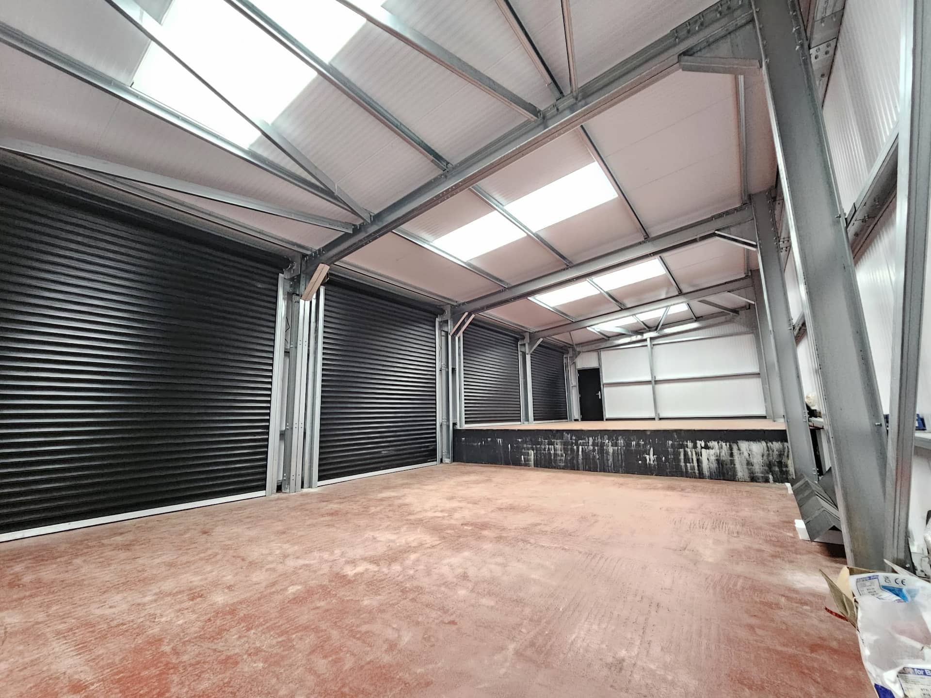 Inside a commercial warehouse showing the internal mechanisms and heavy-duty tracks of newly installed black steel roller doors.