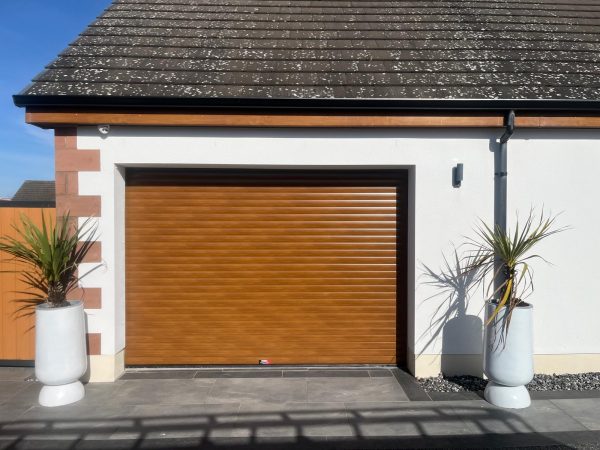 Golden oak woodgrain finish insulated residential roller garage door fitted to a modern white rendered home.